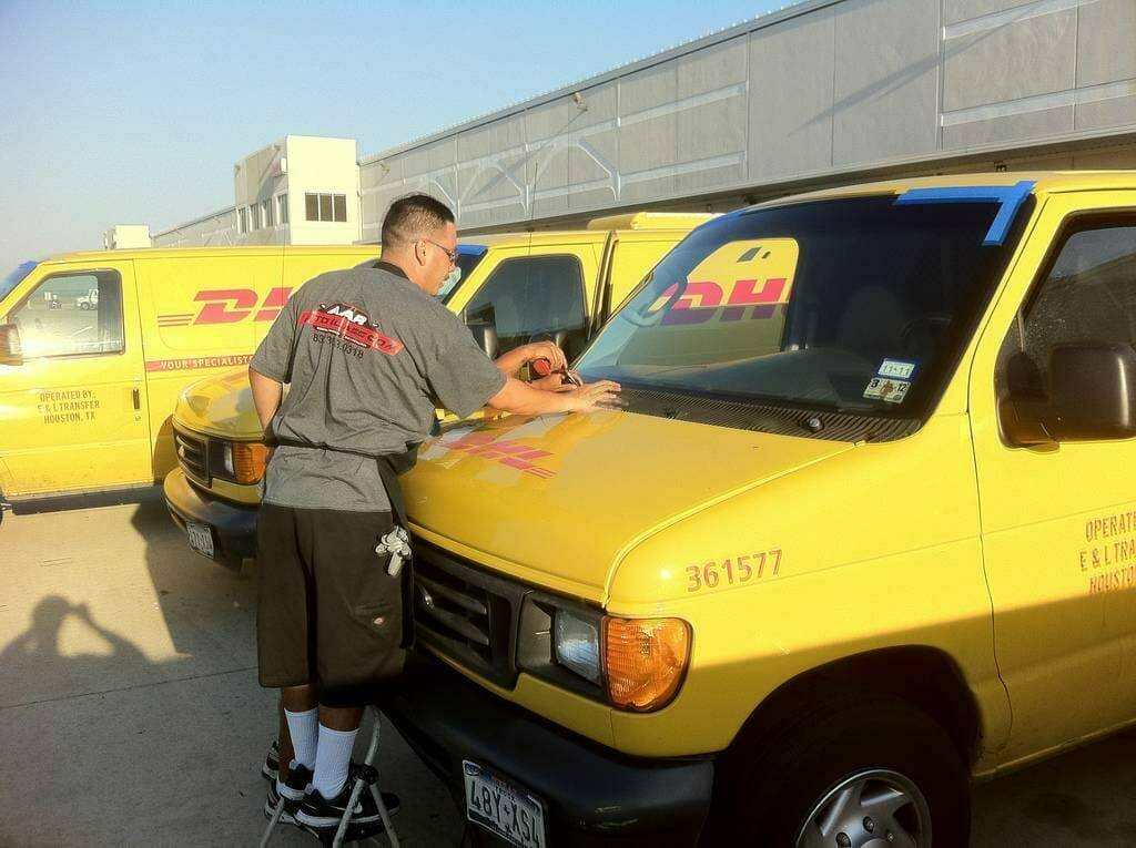 This snapshot showcases our skilled team in action, efficiently replacing front windshields on five DHL Express Shipping vans. These company vehicles, parked in a large lot at the DHL premises in Highland Hills, Texas, suffered damage from flying road debris, necessitating a full windshield replacement. The scene represents our commitment to prompt and professional service for commercial fleet vehicles.