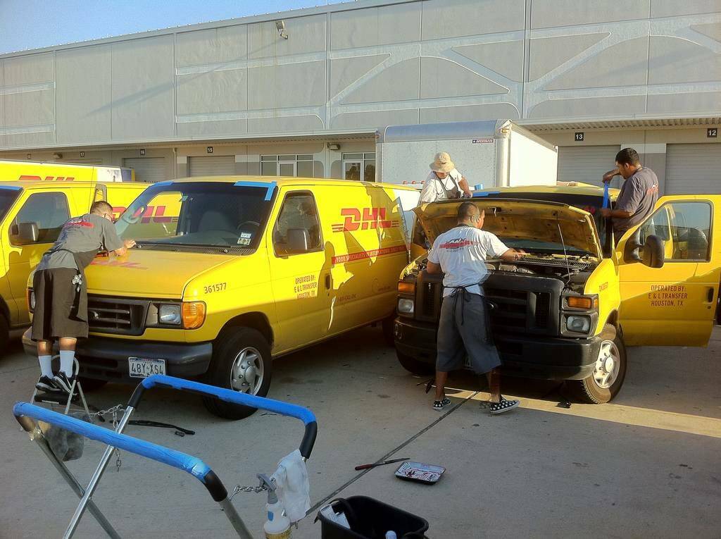 In this image, five of our diligent technicians are depicted replacing the front windshields of a fleet of DHL Express Shipping vans. The windshields were damaged due to road debris during delivery operations and required full replacements. The photo was taken during a commercial auto glass appointment in Highland Hills, Texas, highlighting our team's capacity to handle large-scale fleet vehicle servicing.
