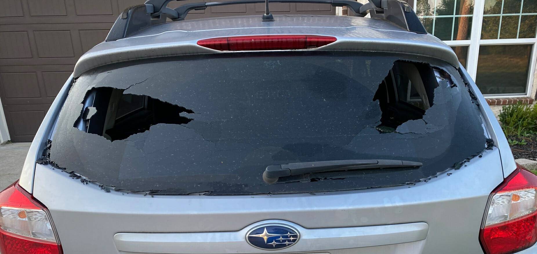 The image captures a 2018 Subaru Forester SUV parked in Lackland AFB, San Antonio, Texas. The vehicle's rear windshield, originally featuring factory privacy tint, is visibly broken as a result of vandalism. A full replacement is required and a home auto glass appointment has been scheduled to facilitate the necessary repairs and restore the vehicle's rear visibility.
