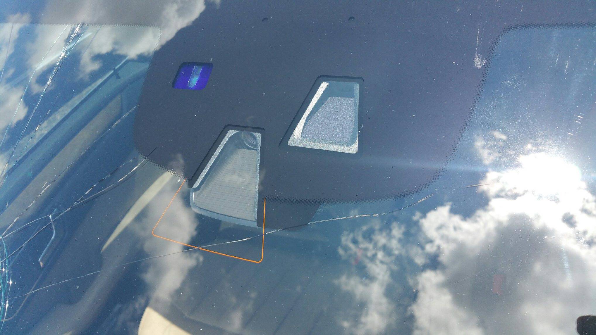 Close-up of openings for windshield-mounted equipment near the rearview mirror, with cracked glass nearby.