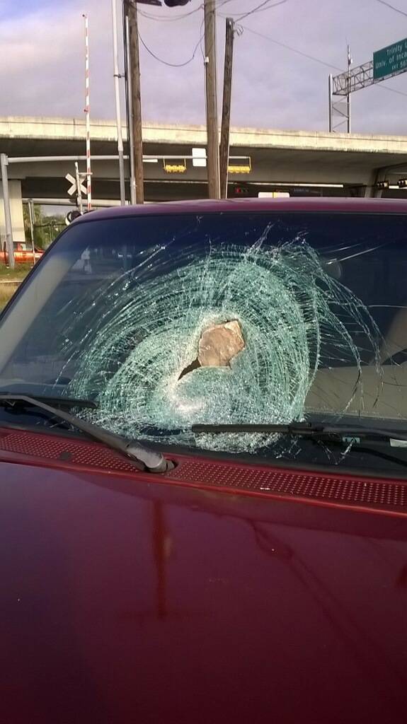 A large rock lodged in the cracked front windshield of a red pickup truck.