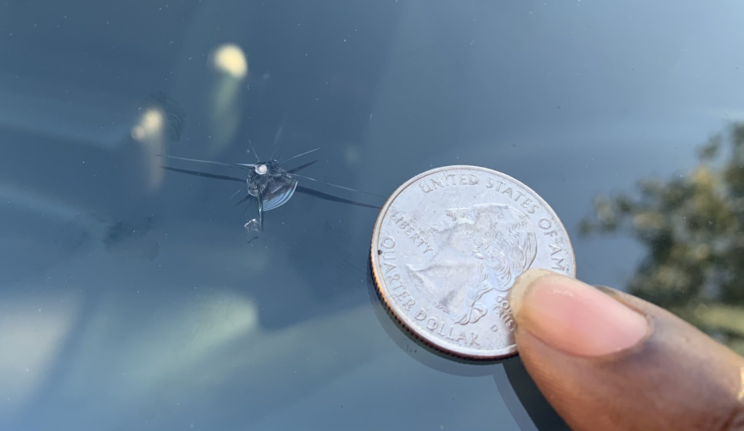 Close-up of a glass chip with short radiating cracks and a quarter held beside it.