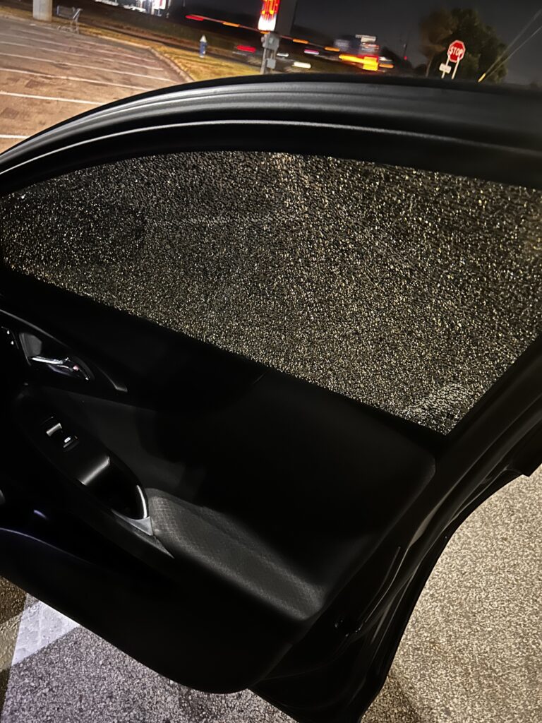 Open vehicle door with its side-window glass broken into many small fragments.